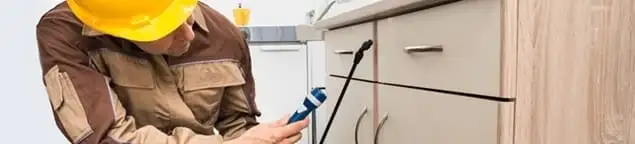 Roach exterminator applying treatment under kitchen cabinets in Wilmington, NC