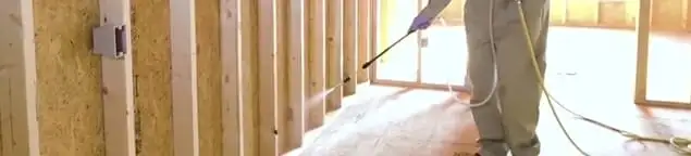 Termite treatment technician applying spray along framing and unfinished walls in Wilmington, NC